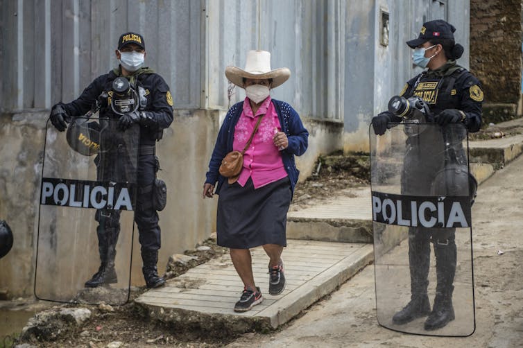 Woman in cowboy hat walks on a street lined with police