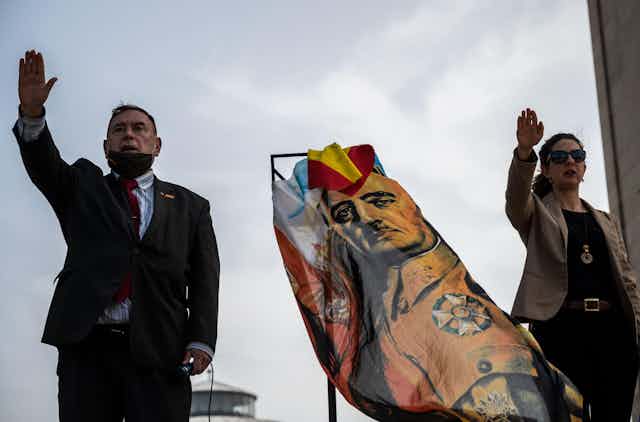 A man and a woman give the fascist salute next to a flag with the image of Spanish dictator Francisco Franco, March 2021.