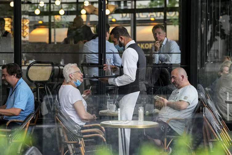 A waiter wearing a face mask to protect against coronavirus serves at a restaurant terrace in Paris
