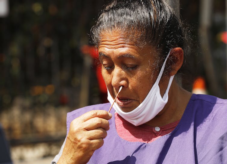 mulher com máscara baixa esfrega o próprio nariz