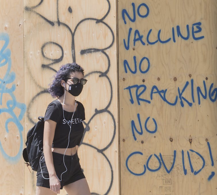 Une femme porte un masque de protection alors qu’elle passe devant un graffiti anti-vaccins
