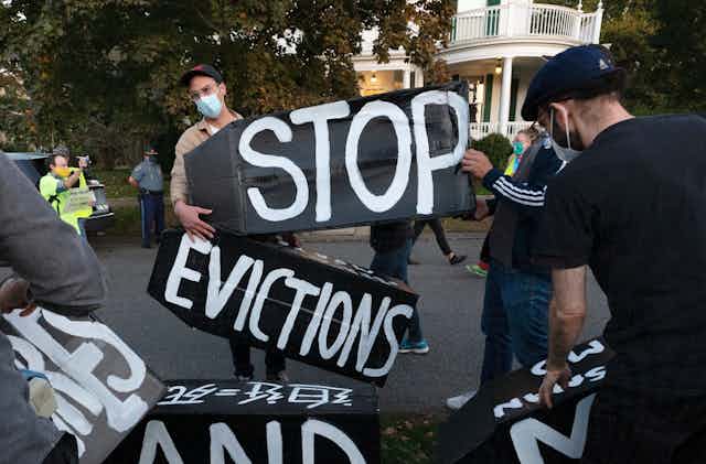 Protestors wearing masks hold up several signs that together say 'stop evictions' 
