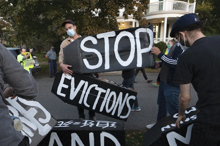 Protestors wearing masks hold up several signs that together say 'stop evictions'