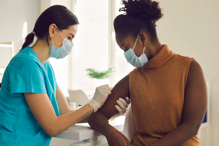 A young health provider vaccinates another young woman.