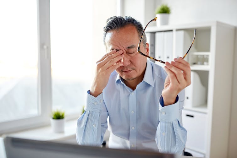 Man in a home office takes his glasses off and rubs his eyes.