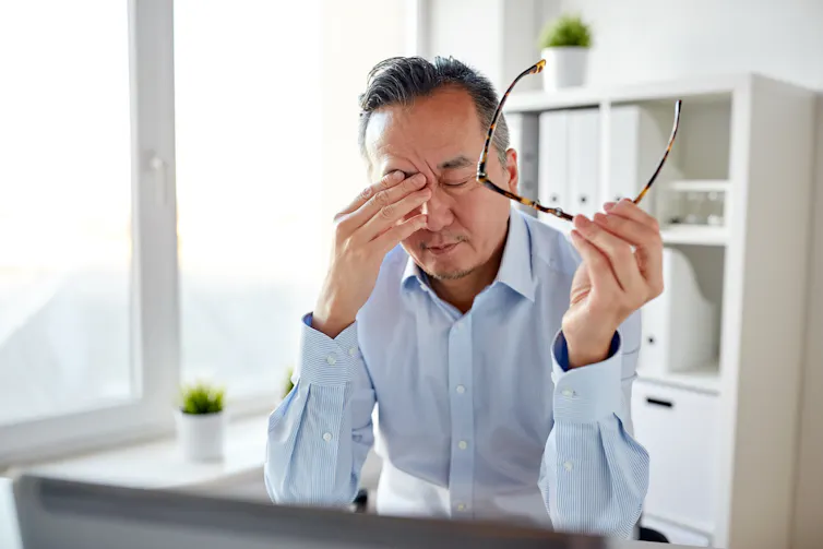 Man in a home office takes his glasses off and rubs his eyes.