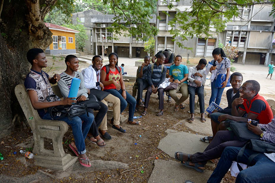 Young women and men (students) seated under a tree, discussing happily.