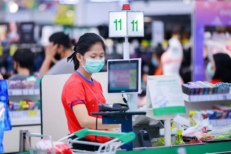 A masked supermarket check out operator scans products.