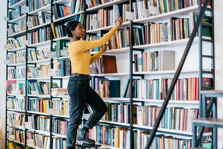 Woman taking books down from a shelf in the library.