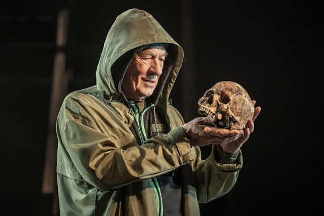 Man in hooded coat looks at a skull.