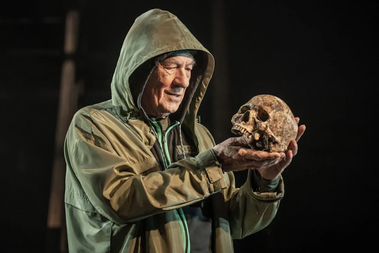 Man in hooded coat looks at a skull.