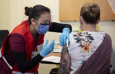 A nurse wearing a mask vaccinates a woman with tattoos on her arm.