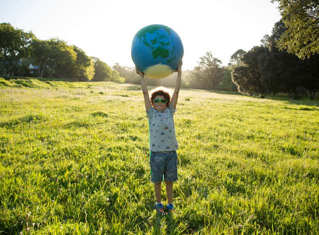 Young boy wearing sunglasses in field holding a globe above his head. 