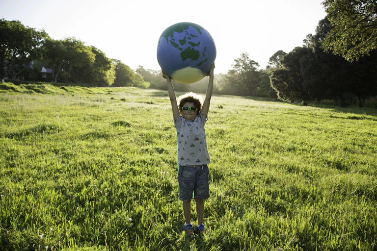 Young boy wearing sunglasses in field holding a globe above his head.