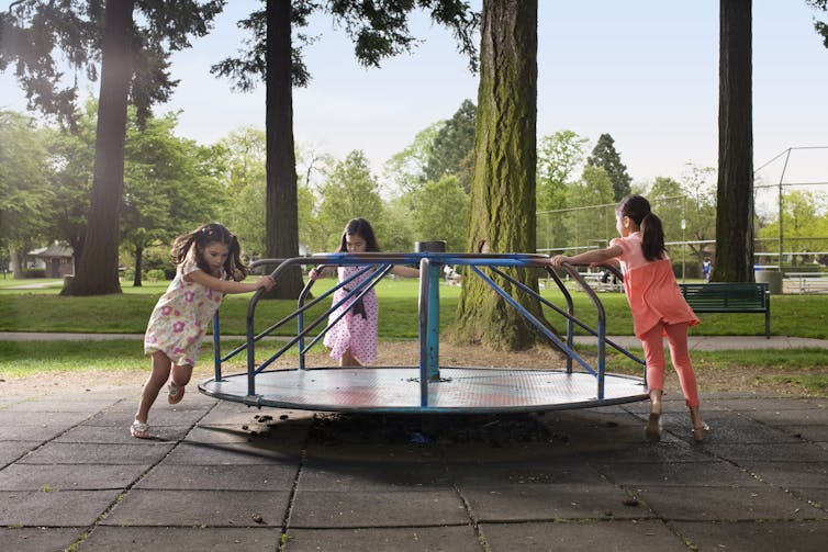Three young girls playing on a playground carousel