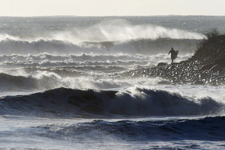 A surfer walking along the shore in the wake of a hurricane