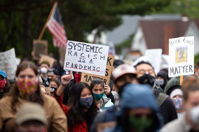 Photo of a protest, man holds a sign that reads 'systemic racism is a pandemic'