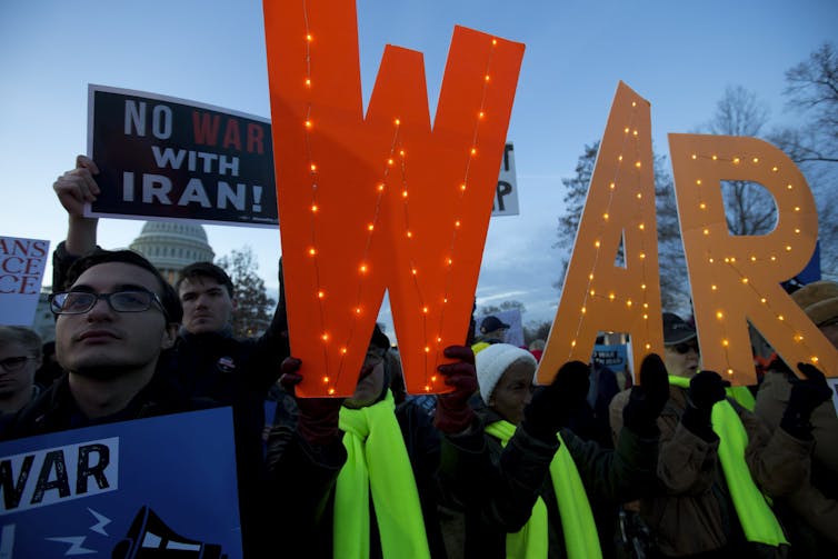 Demonstrators hold signs opposing war.