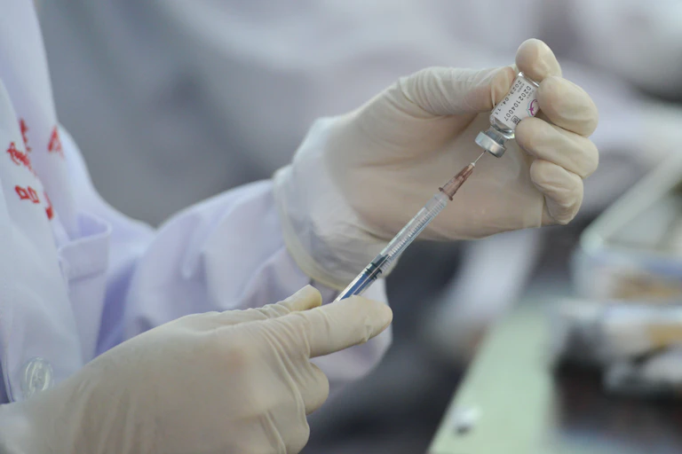 A pair of hands and latex gloves holds a syringe pressed into a drug vial