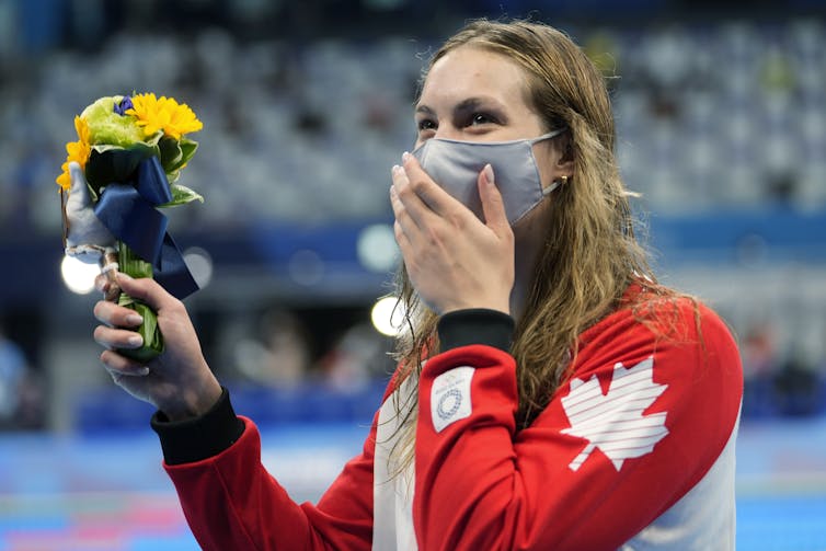 Woman holding a bouquet of flowers beams from behind a medical face mask.