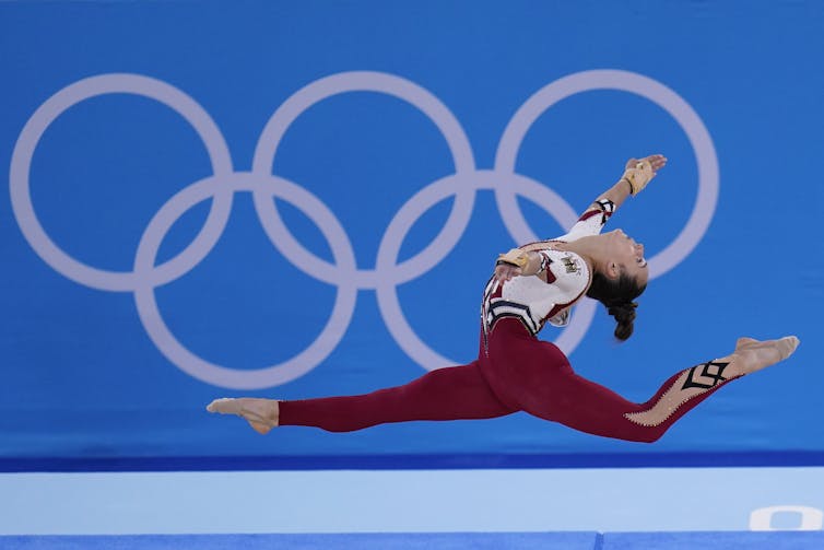 Woman in full unitard doing a split jump in midair.