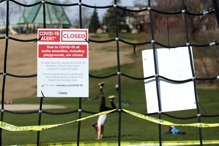 A sign about parks being closed due to COVID-19 with a person doing a handstand in the park in the background
