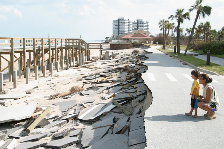 A mother and young son look at pavement eroded and a collapsed road