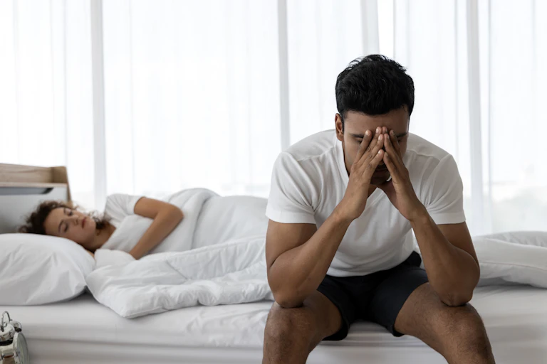 Un hombre angustiado se sienta a un lado de su cama.
