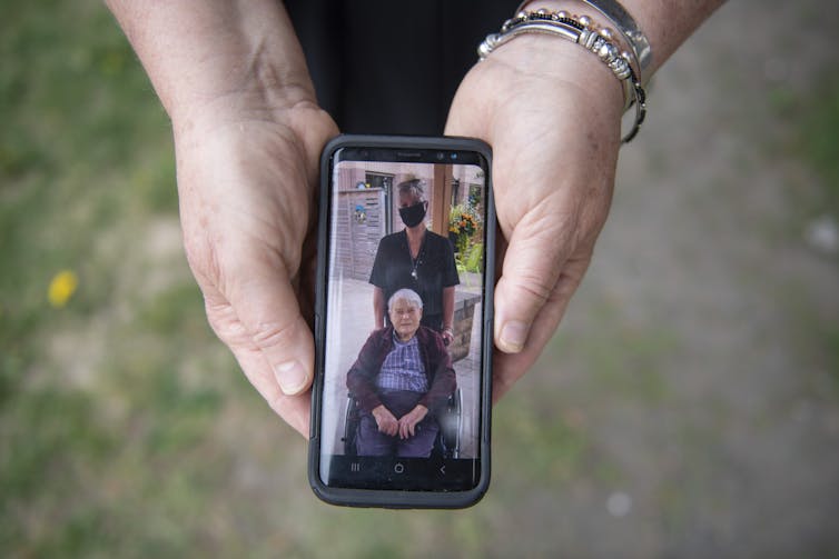 A smartphone in a woman's hands, showing a picture of a woman in a mask and a man in a wheelchair