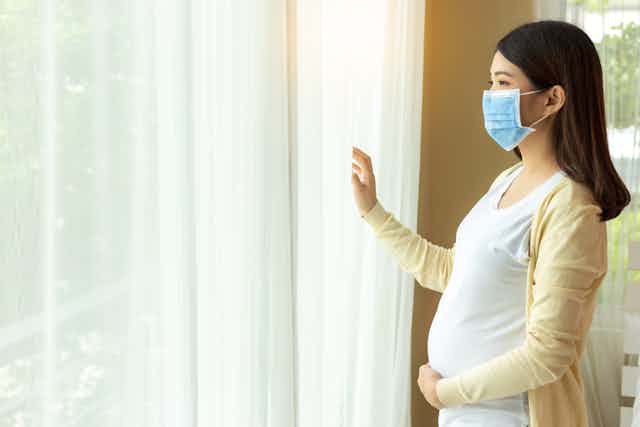 Pregnant woman looks out her loungeroom window.