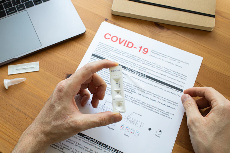 A hand holds a rapid antigen test in front of an information sheet.