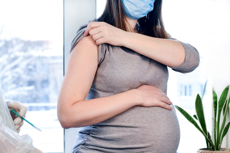 Pregnant woman in a mask rolls up her sleeve to be vaccinated.
