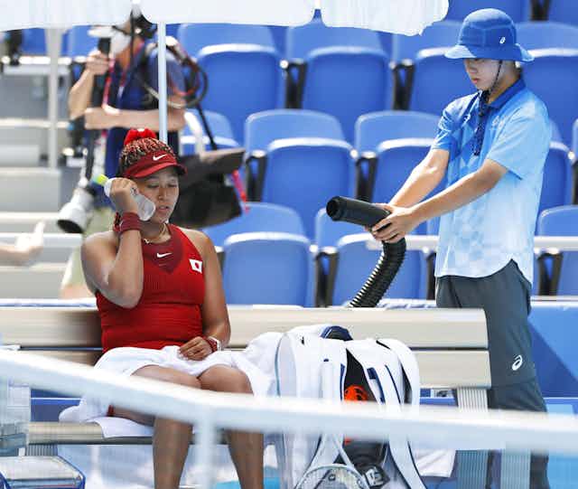 Tennis player Naomi Osaka holds an iced water bottle to her cheek during a cooling break