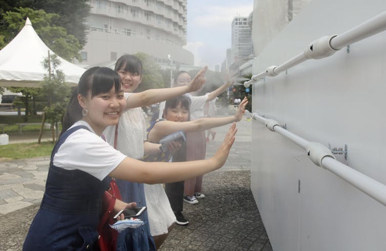 Girls stand at a misting station at the beach volleyball Olympic venue in Shiokaze Park, Tokyo