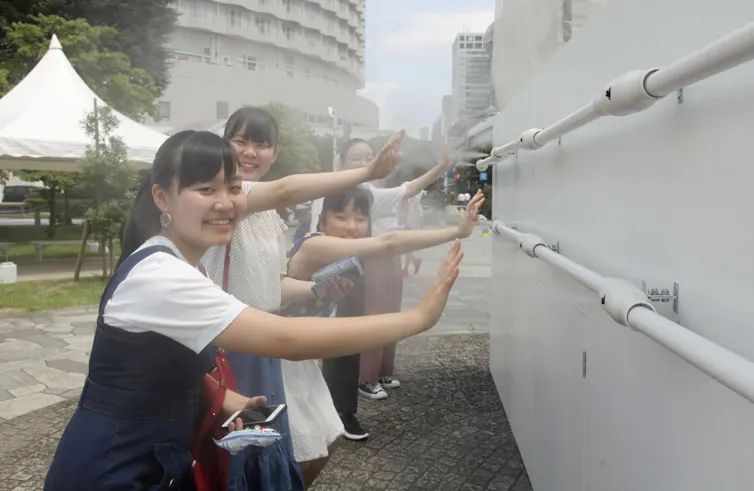 Girls stand at a misting station at the beach volleyball Olympic venue in Shiokaze Park, Tokyo