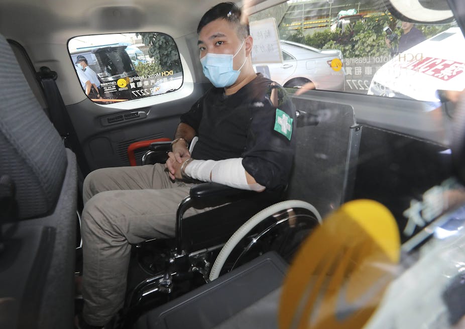 Tong Ying-kit, wearing a face mask, sitting in a wheelchair in the back of a van as he arrives to court.