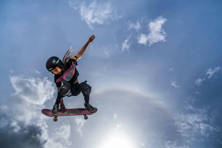 Skateboarder Sky Brown in mid-air against a blue, cloud-filled sky