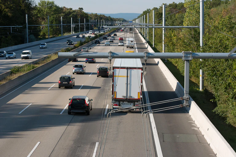 Overhead power lines on a motorway with lorries beneath.