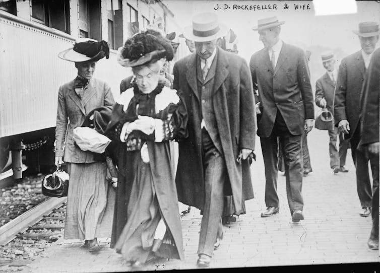 Wealthy people walk alongside a train in the early 1900s