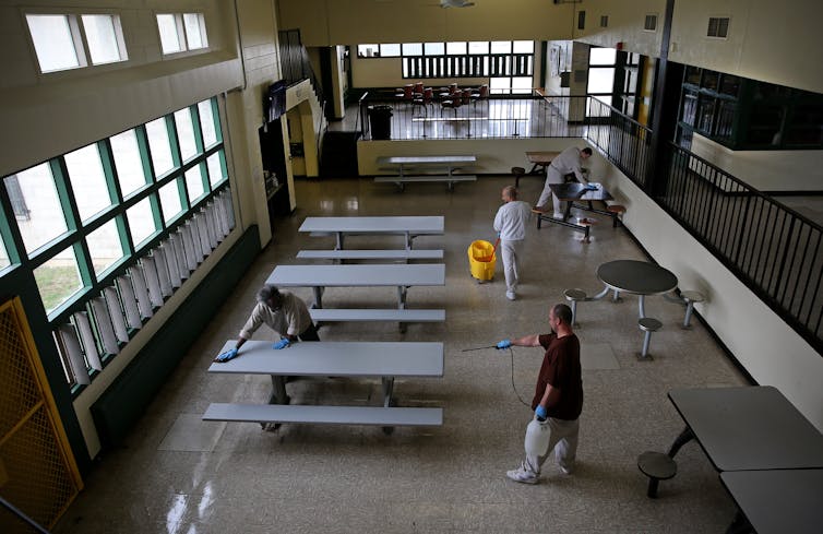 People clean and spray a room with picnic tables and seats.