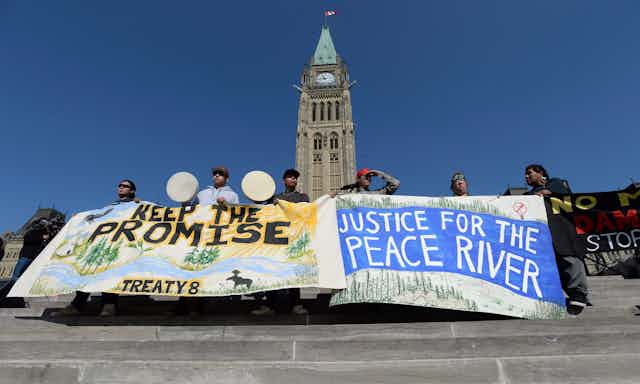 People stand in front of parliament hill holding banners that read 'keep the promise treaty 8' and 'justice for the peace river'