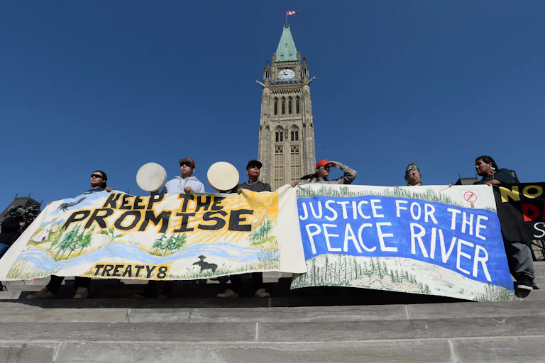 People stand in front of parliament hill holding banners that read 'keep the promise treaty 8' and 'justice for the peace river'