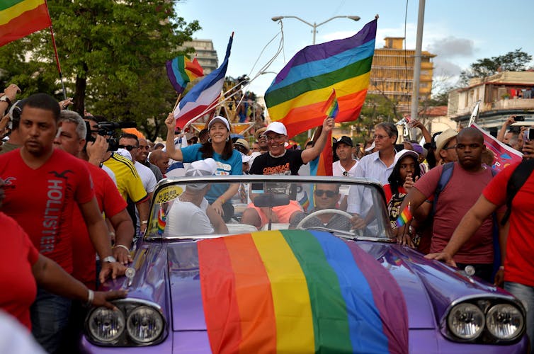Mariela Castro rides in a car decked out in pride flags surrounded by crowds in a pride parade
