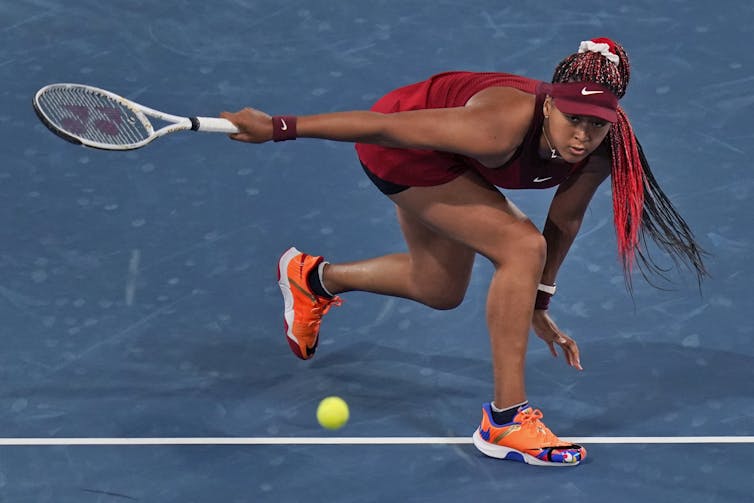 Woman player crouched with a tennis racquet in one hand after returning a hit.