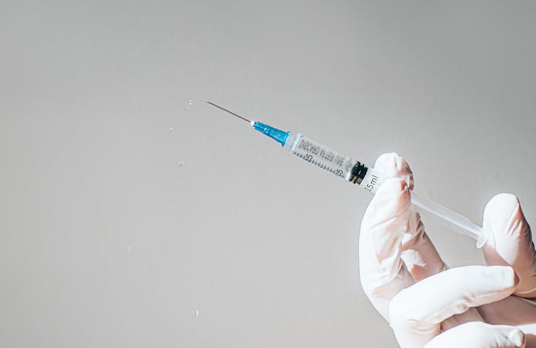 A gloved hand holding a syringe filled with clear liquid