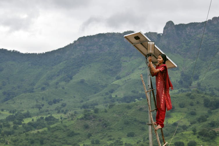 A woman standing on a ladder making adjustments to a solar panel