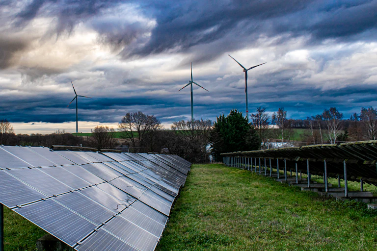 A small array of solar PV panels with wind turbines in the background