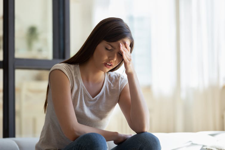 Despairing girl sits on bed with hand to her head