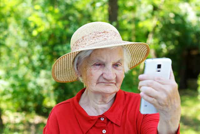 Elderly lady wearing hat looking confused at smartphone