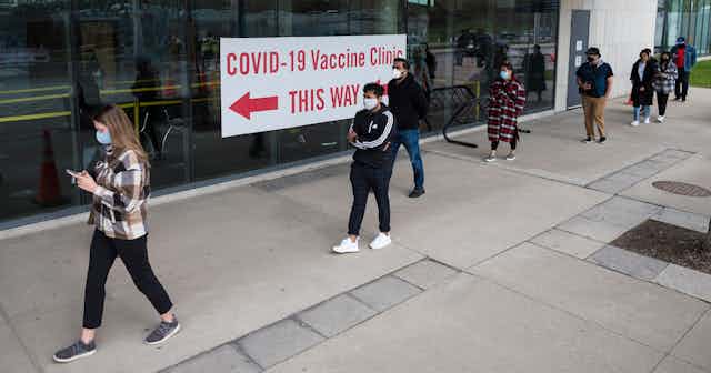 People stand in a line in front of a 'COVID-19 vaccine clinic' sign